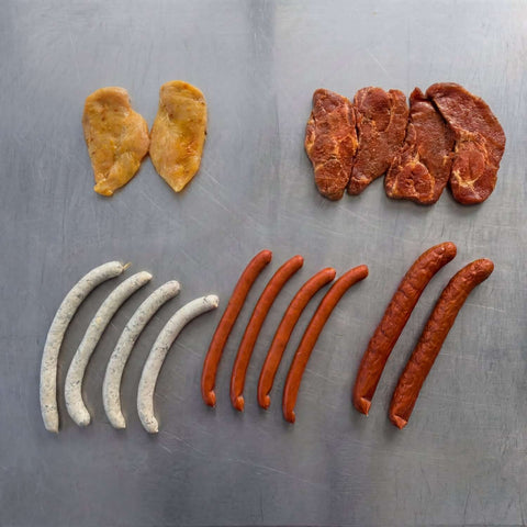 Probierpaket Grillmix mit Gourmet-Würsten, Chili-Krainern, Halsgratsteaks, Hähnchenbruststeaks und Cabanossy, übersichtlich auf Edelstahl angerichtet.
