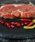 Rohes Entrecôte-Steak auf schwarzer Schieferplatte mit Chili und Lauchstreifen