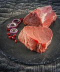 Zwei Stücke rohes Rinderfilet auf einer runden Schieferplatte mit roten Zwiebelringen und Granatapfelkernen