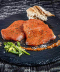 Zwei marinierte Schweinelenden-Steaks auf runder Schieferplatte mit Frühlingszwiebeln, Gewürzen und Brot