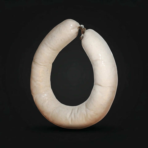 Weiße Bratwurst im Ring, roh und frisch hergestellt, traditionell gebunden und freigestellt vor dunklem Hintergrund